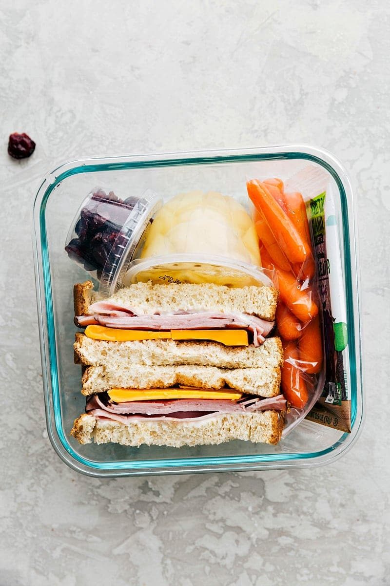 A meat and cheese sandwich, fresh fruit, veggies, and a snack, all packed in a container and ready to go.