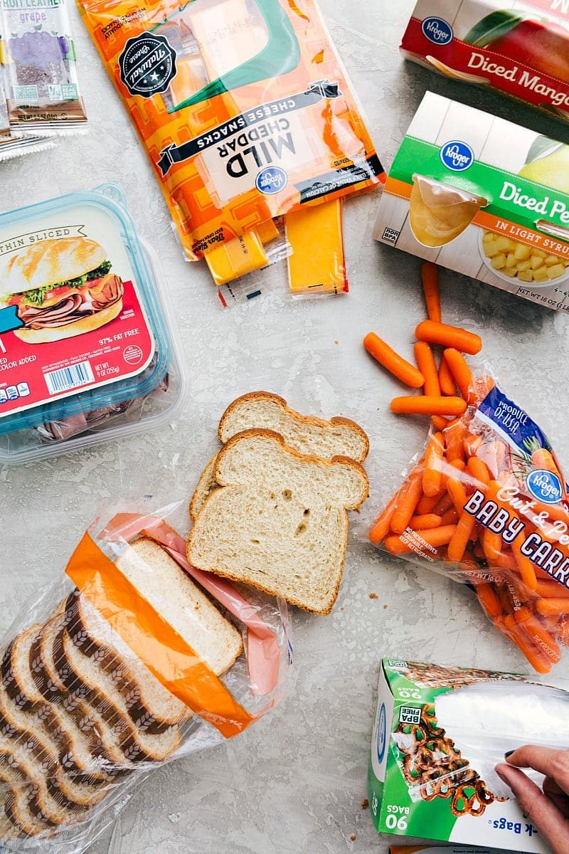 Sliced deli meat, cheese, fruit, bread, veggies, and a fruit snack, all packed together for a nutritious and balanced school lunch idea for kids.