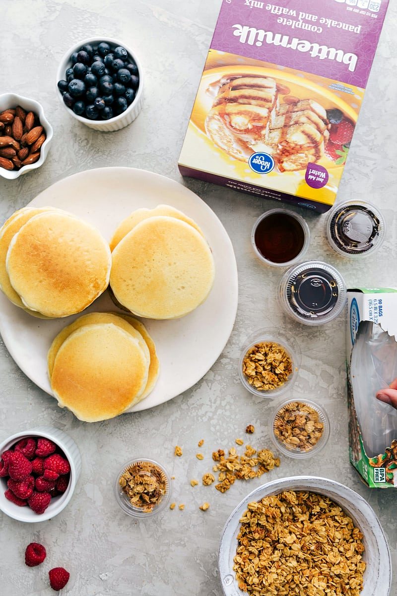 Pancakes with toppings such as granola, fruit, and nuts, with syrup in containers, ready to make a reliable lunch as part of kids school lunch ideas.