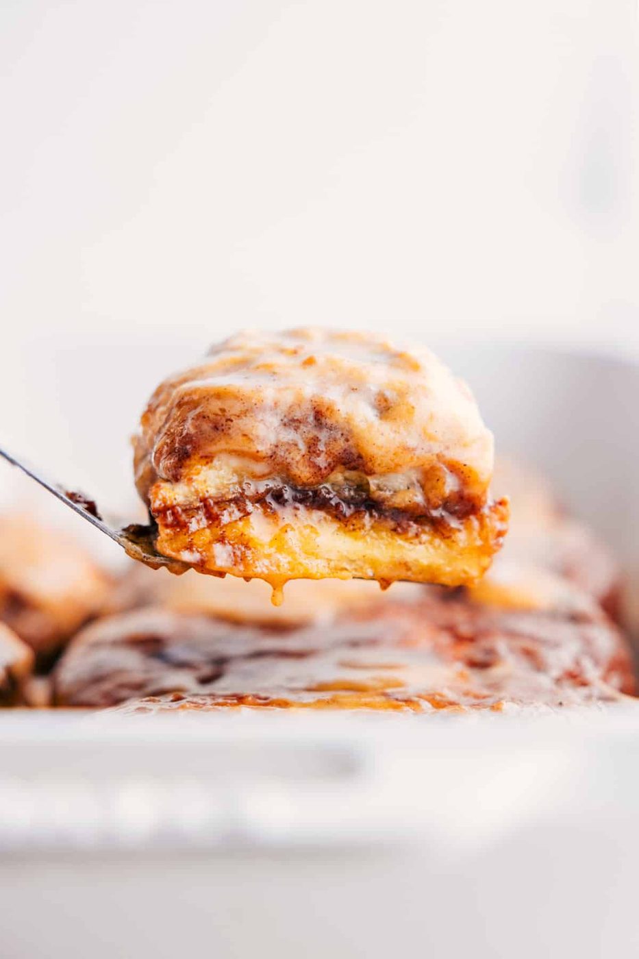 Magic pumpkin cinnamon rolls being pulled from the pan, drizzled with cream cheese glaze and ready to enjoy.