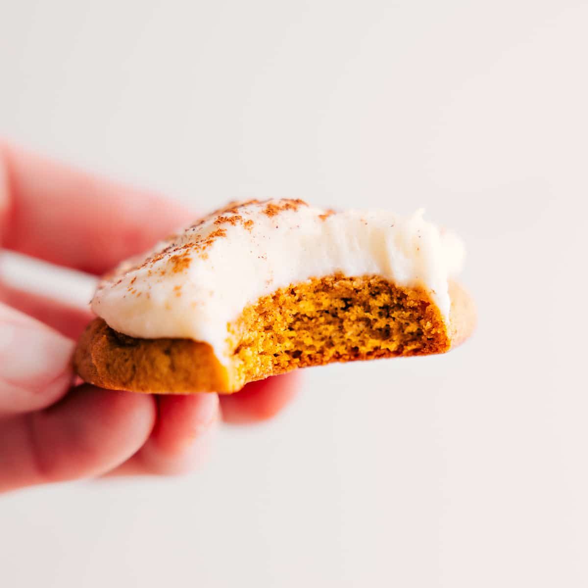 A pumpkin cookie with cream cheese frosting and a bite taken out.