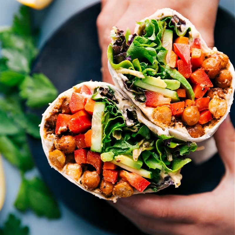 Hummus wrap cut in half, showing chickpeas, fresh veggies, and sauce inside.