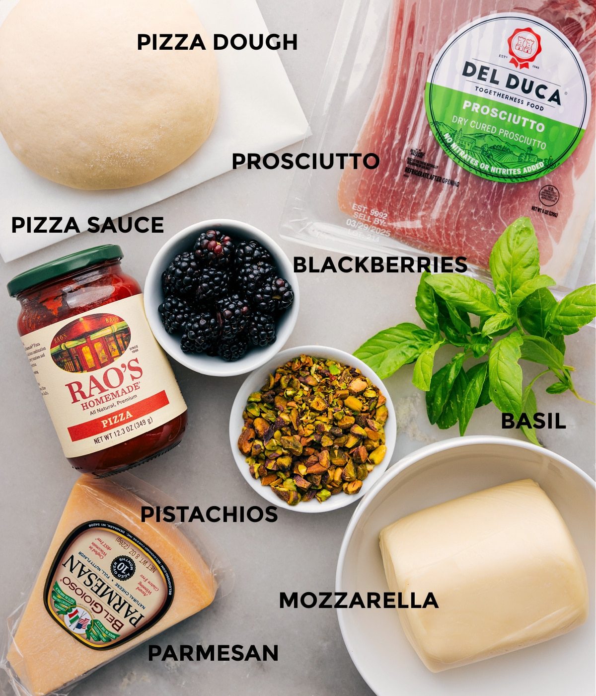 All the ingredients for this recipe are prepped and ready for straightforward assembly, including the dough, prosciutto, herbs, berries, sauce, cheese, and pistachios.