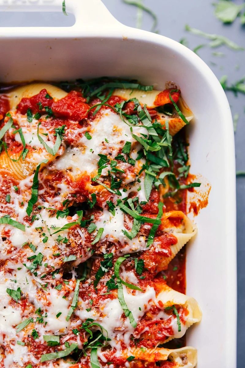 A pan of stuffed shells with sausage, topped with melted cheese and a basil chiffonade, presenting a warm and satisfying meal suitable for any occasion.