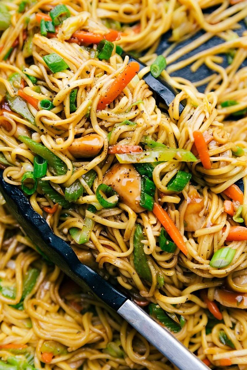 Chicken chow mein in a skillet with tongs, filled with fresh vegetables, evenly cooked and seasoned.