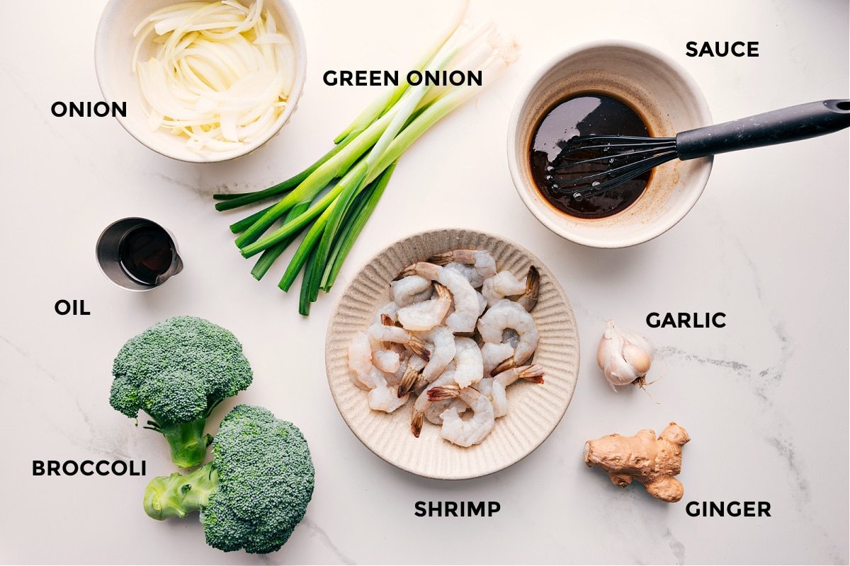 All the ingredients in this recipe prepped out for straightforward assembly including the onion, oil, broccoli, shrimp, green onion, sauce, garlic, and ginger.