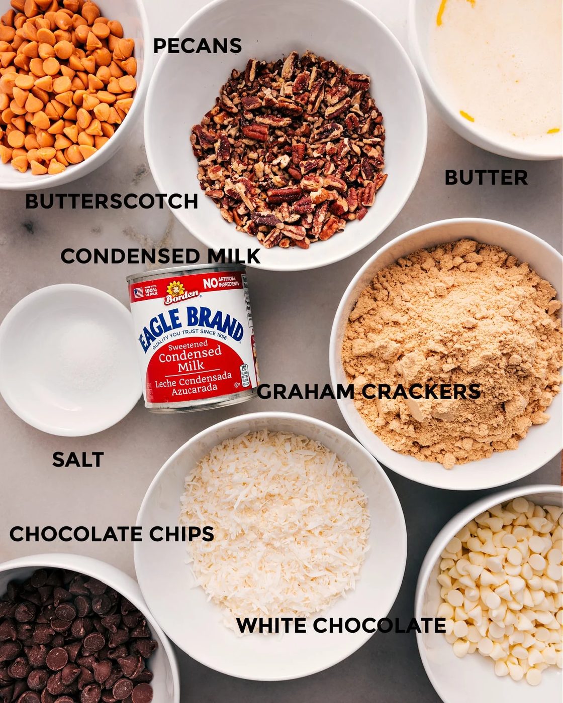 All the ingredients prepped for straightforward assembly—butter, butterscotch, pecans, condensed milk, graham crackers, salt, coconut, and chocolate chips.