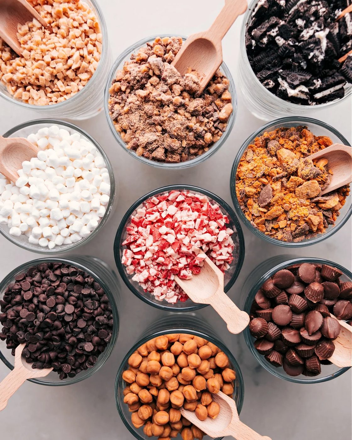 Array of toppings in small glass bowls for a hot chocolate bar, including marshmallows, chocolate chips, and sprinkles.