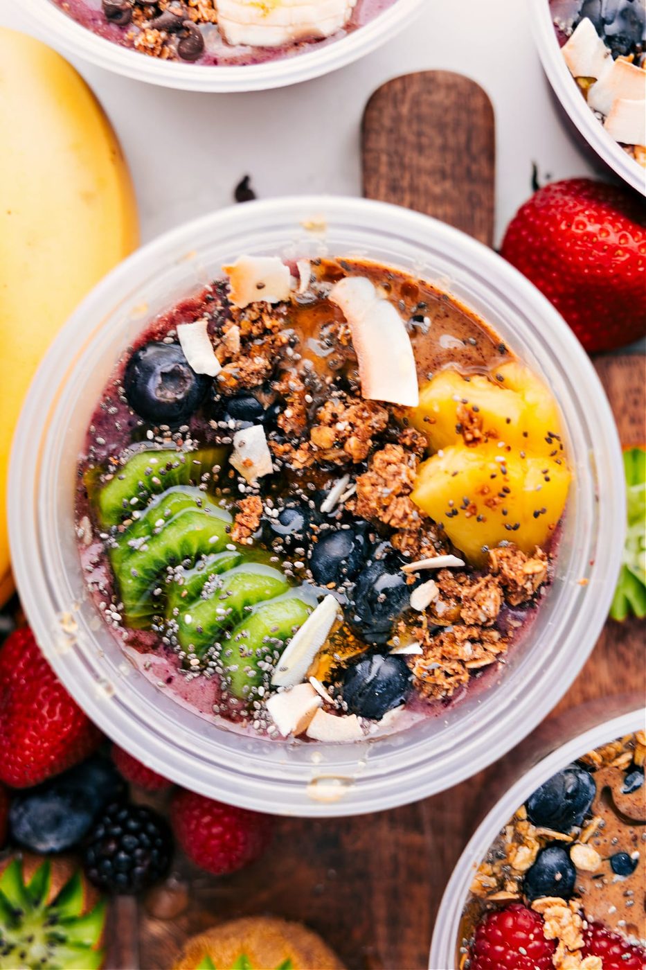 Tropical acai bowls recipe with kiwi, blueberries, pineapple, coconut flakes, granola, chia seeds, and honey.