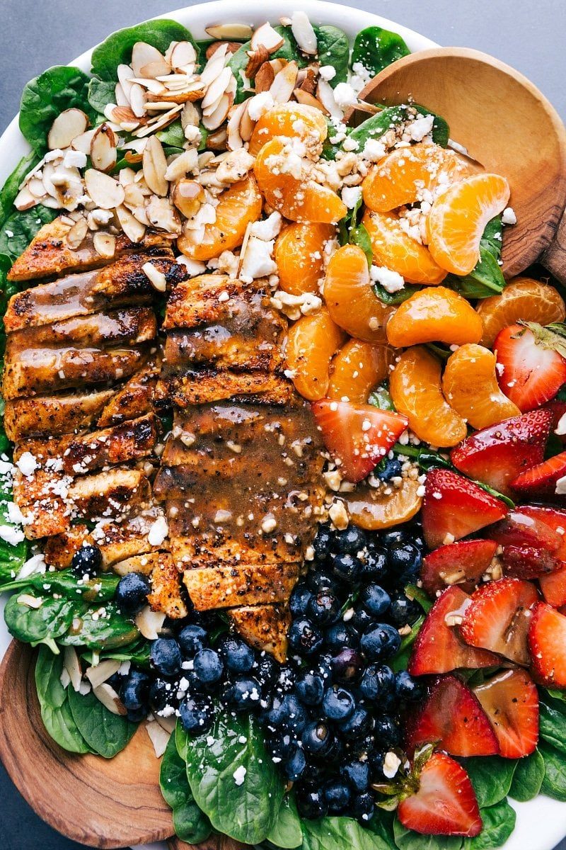 Completed spinach chicken salad showcasing sliced chicken, spinach, topped with fruit, dressing, and nuts, epitomizing a healthy and satisfying meal.