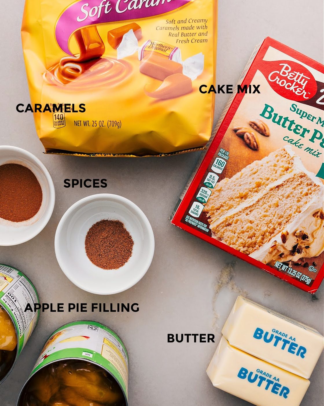 All the ingredients for this recipe are set out for straightforward assembly, including caramels, cake mix, spices, butter, and pie filling.