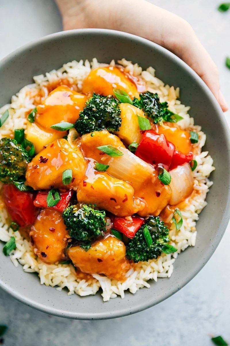 Baked sweet and sour chicken on a bed of rice with fresh green onions on top.