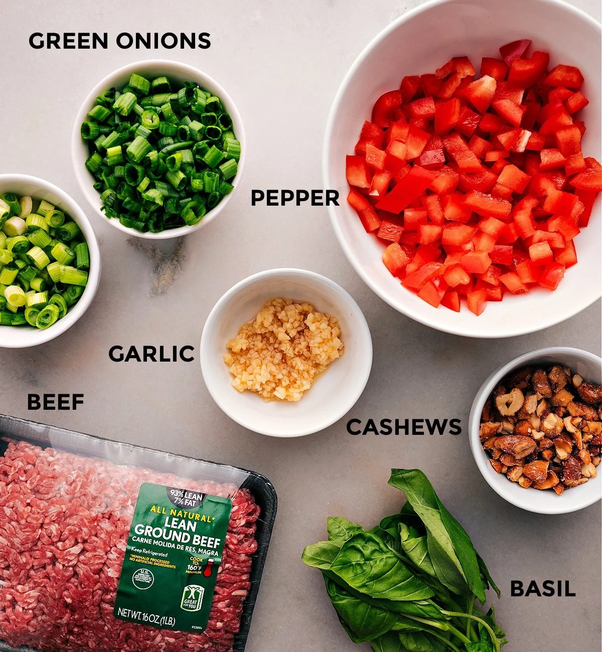 All the ingredients for this recipe are prepped and ready for straightforward assembly, including peppers, garlic, meat, cashews, and basil.