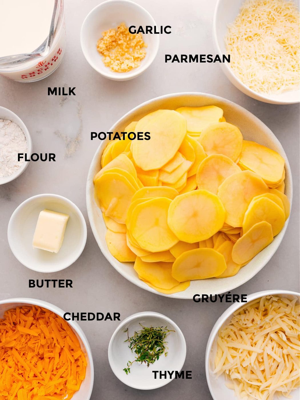 The ingredients for this recipe—potatoes, flour, butter, thyme, cheese, milk, and garlic—are prepped and ready for straightforward assembly.