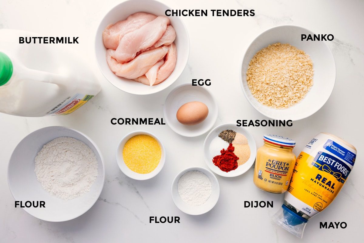 All the ingredients in this recipe prepped out for straightforward assembly including buttermilk, flour, cornmeal, flour, meat, egg, flour, seasoning, dijon, mayo, and panko.