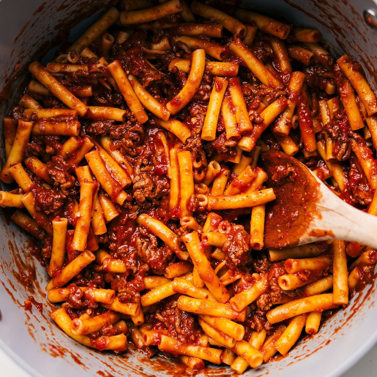 Cooked pasta being tossed with the rich meat sauce.