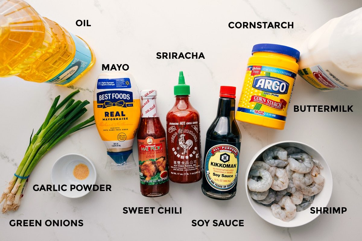 All the ingredients in this recipe prepped out for straightforward assembly including the oil, garlic powder, green onions, mayo, sweet chili, sriracha, soy sauce, cornstarch, buttermilk, and shrimp.