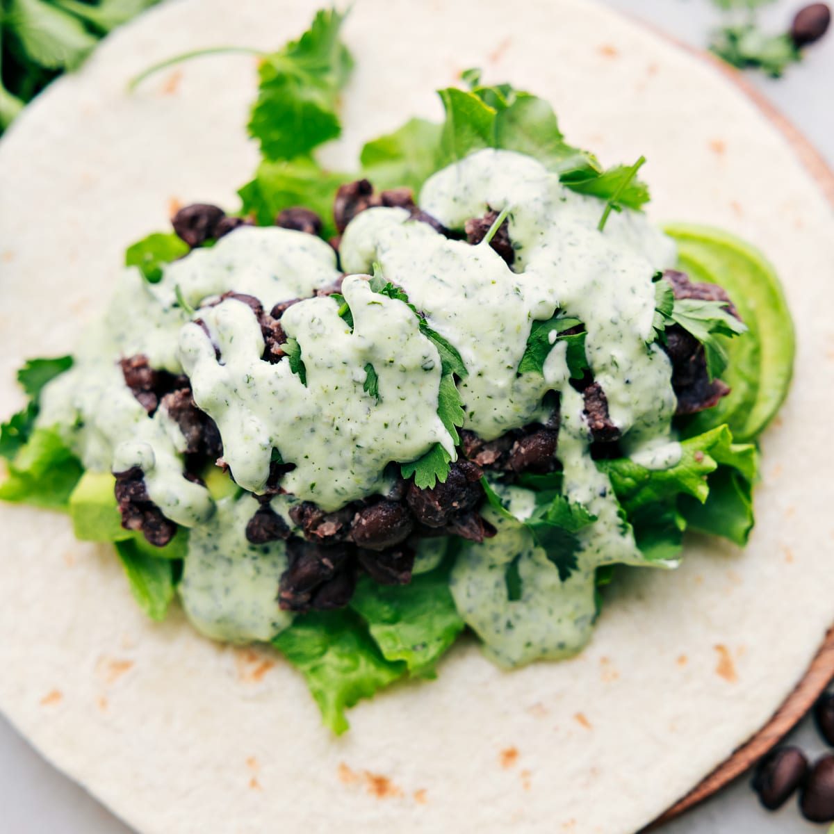 A black bean wrap, opened up to reveal the satisfying filling of avocado, lettuce, black beans, and the most flavorful cilantro lime sauce.