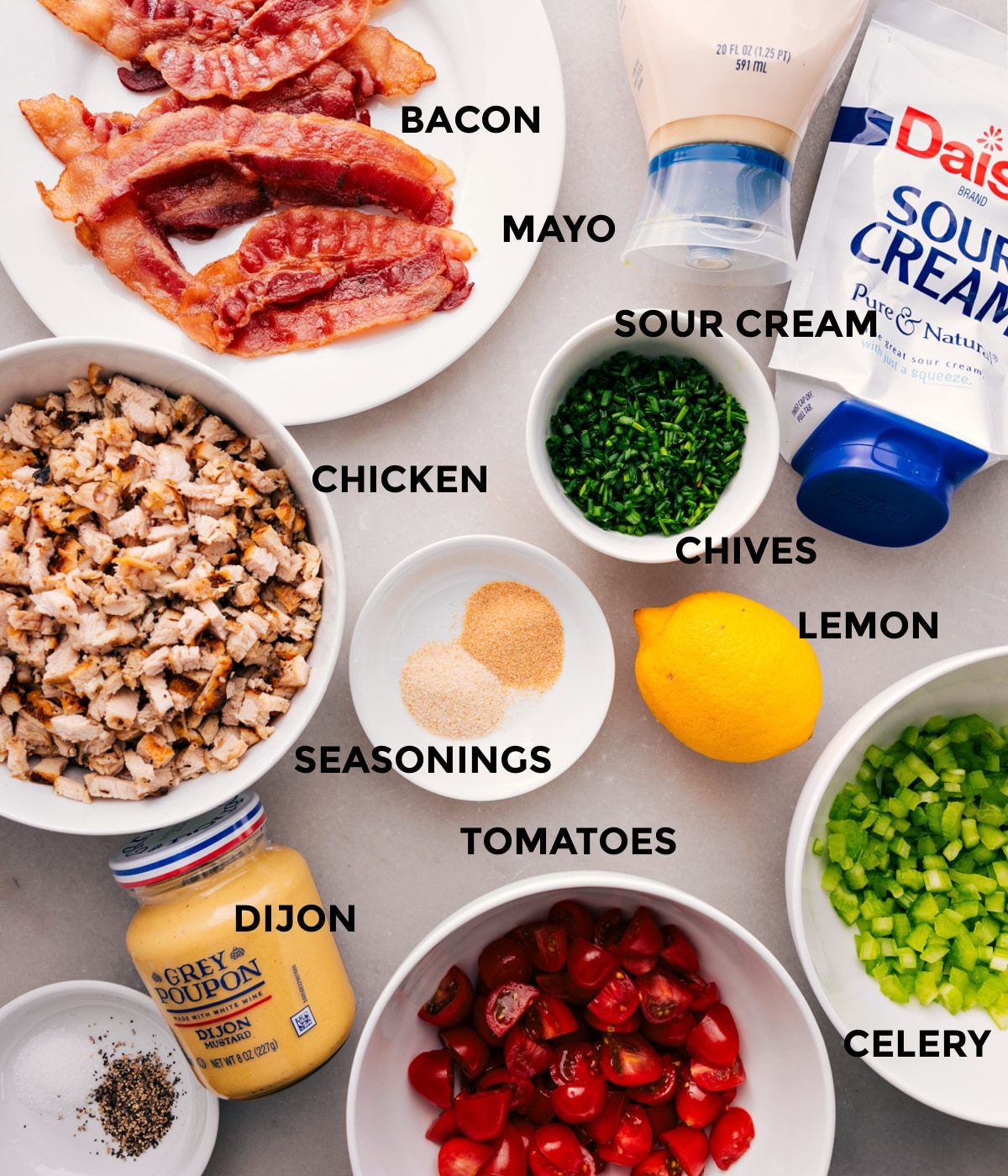 All the ingredients for this recipe are prepped and ready for straightforward assembly, including the meat, mayo, sour cream, chives, seasonings, lemon, celery, tomatoes, and Dijon.