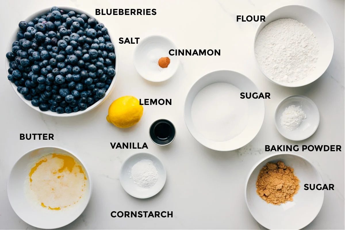 All the ingredients prepped for straightforward assembly: blueberries, salt, cinnamon, flour, sugar, baking powder, cornstarch, lemon, vanilla, and butter.