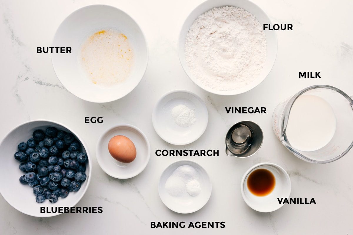 All the ingredients in this recipe prepped out for straightforward assembly including the blueberries, butter, egg, baking agents, cornstarch, flour, milk, vanilla, and a vinegar.