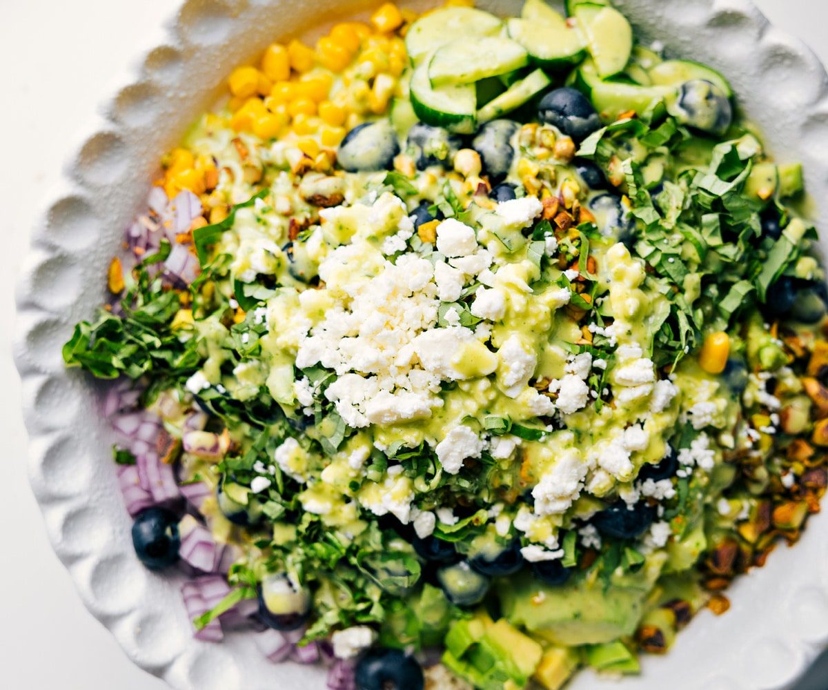Blueberry salad ingredients added to a bowl with dressing drizzled over the top.