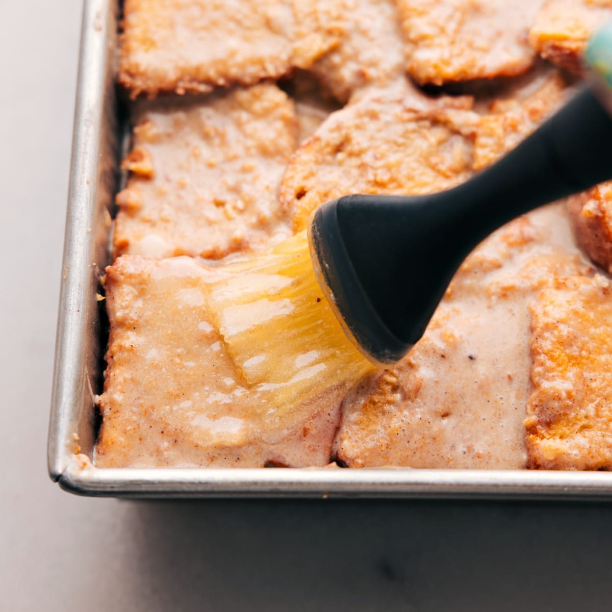 Brushing butter on the top of the dessert in a baking pan, prepped and ready for baking.