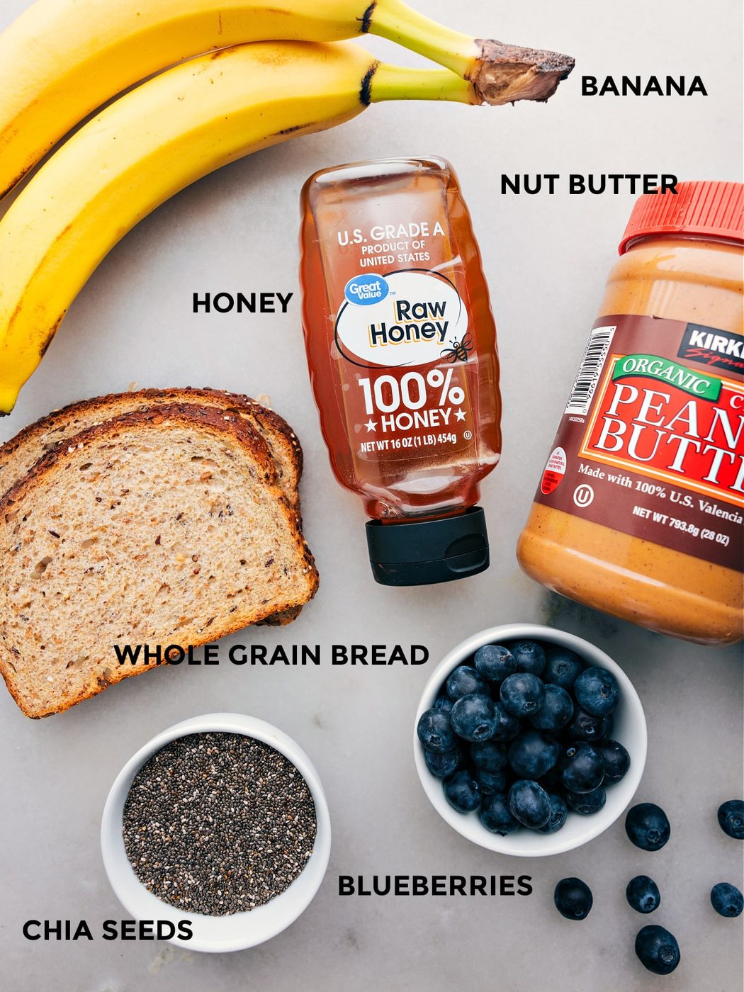 All the ingredients like banana, nut butter, honey, whole grain bread, blueberries, and chia seeds prepped out for straightforward assembly.