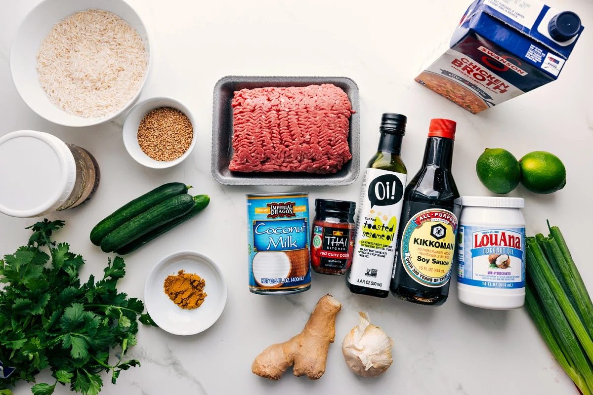 All the ingredients in this recipe prepped out for straightforward assembly including the rice, sesame seeds, cilantro, cucumbers, coconut milk, red curry paste, toasted sesame oil, soy sauce, coconut oil, ginger, garlic, green onions, limes, and broth.