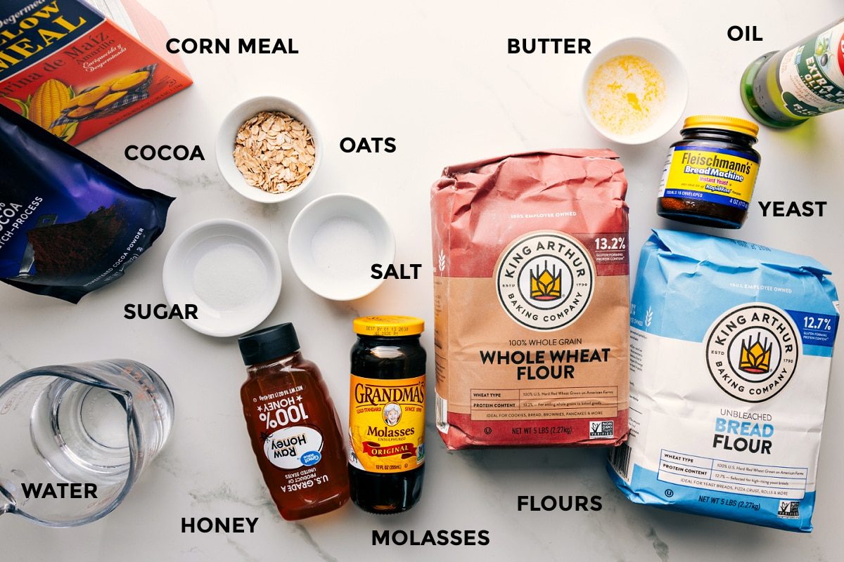 All the ingredients in this recipe prepped out for straightforward assembly including the corn meal, cocoa. sugar, water, honey, molasses, salt, oats, flours, yeast, butter, and oil.