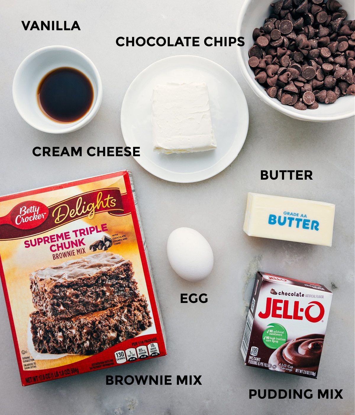All the ingredients in this recipe including the box mix, butter, jell-o, butter, egg, chocolate chips, vanilla, and cream cheese prepped out for straightforward assembly.