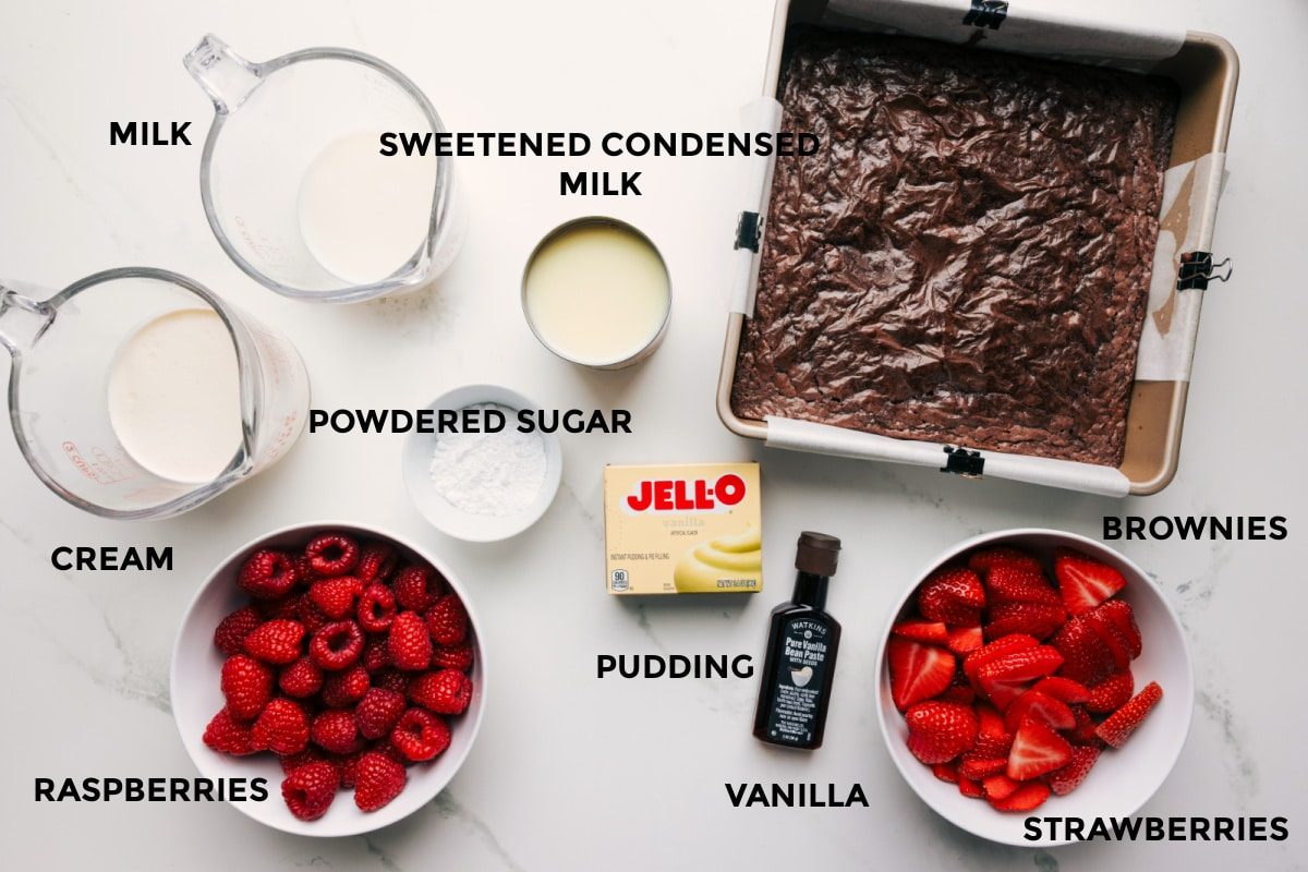 All the ingredients in this recipe prepped out for straightforward assembly including the cream, milk, raspberries, powdered sugar, sweetened condensed milk, pudding, vanilla, strawberries, and brownies.