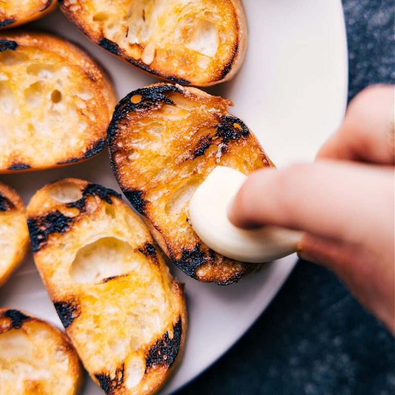 The garlic being spread over the bread for this straightforward Bruschetta recipe.