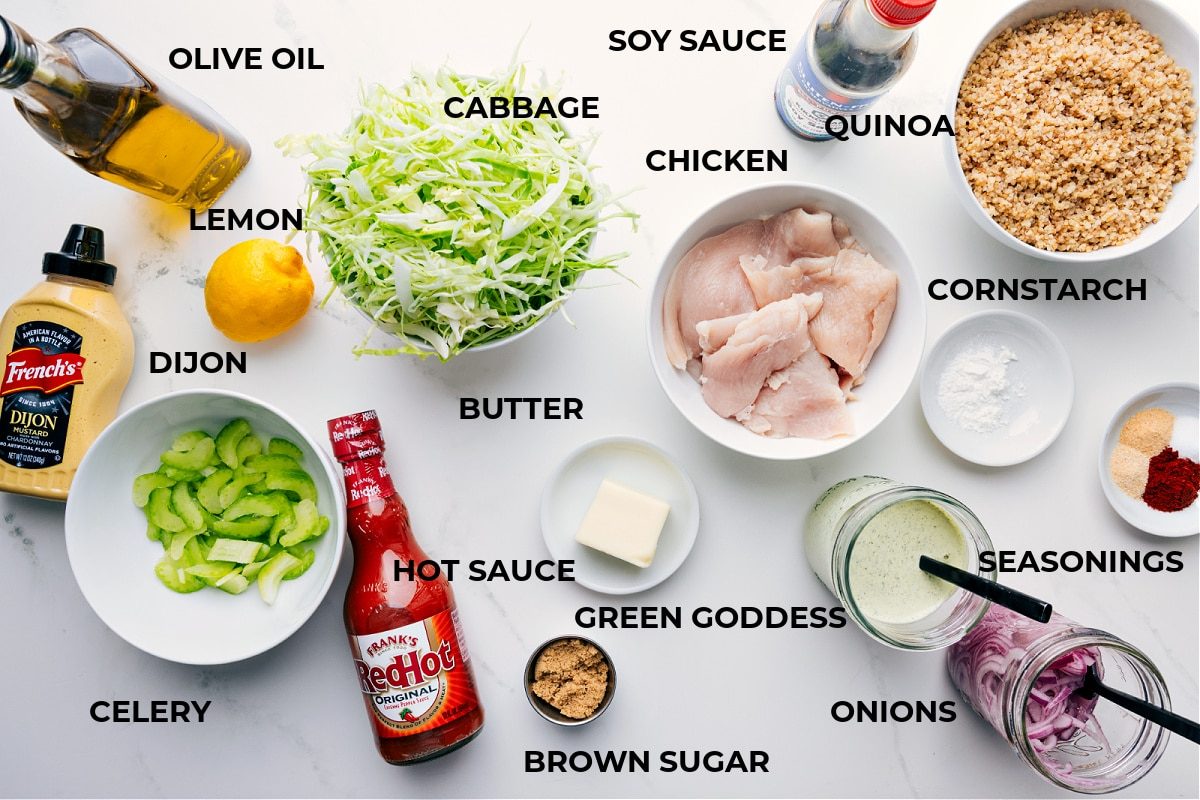 All the ingredients prepped for straightforward assembly, including olive oil, cabbage, chicken, soy sauce, quinoa, cornstarch, seasonings, dressing, onions, butter, hot sauce, celery, Dijon, and lemon.