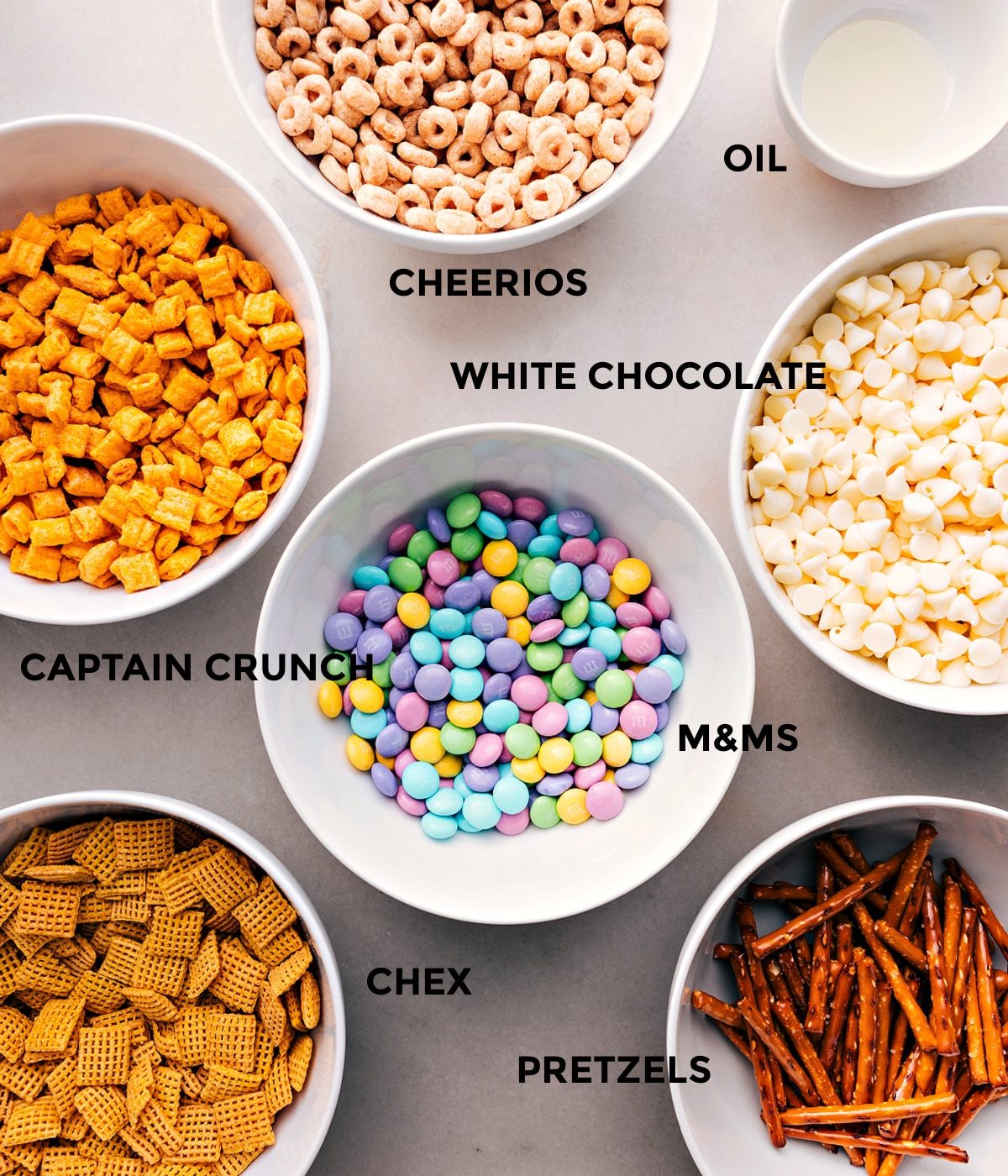 All the ingredients prepped and ready for straightforward assembly—Cheerios, oil, white chocolate, Cap’n Crunch, M&Ms, pretzels, and Chex cereal.