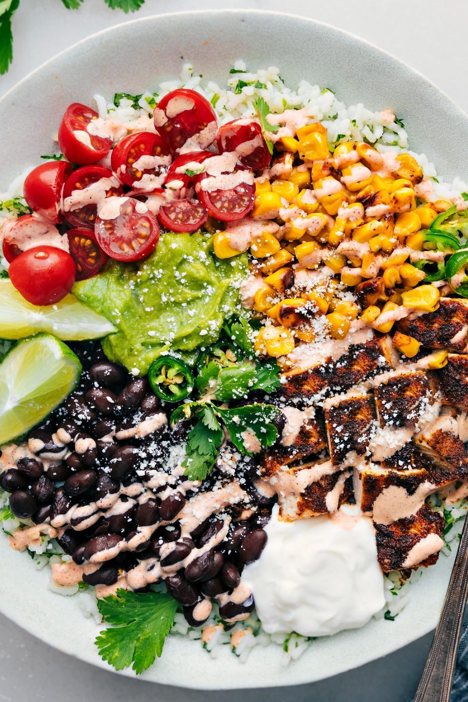Burrito bowl recipe with cilantro-lime rice, black beans, corn, guacamole, tomatoes, and a chili-lime sauce drizzle.