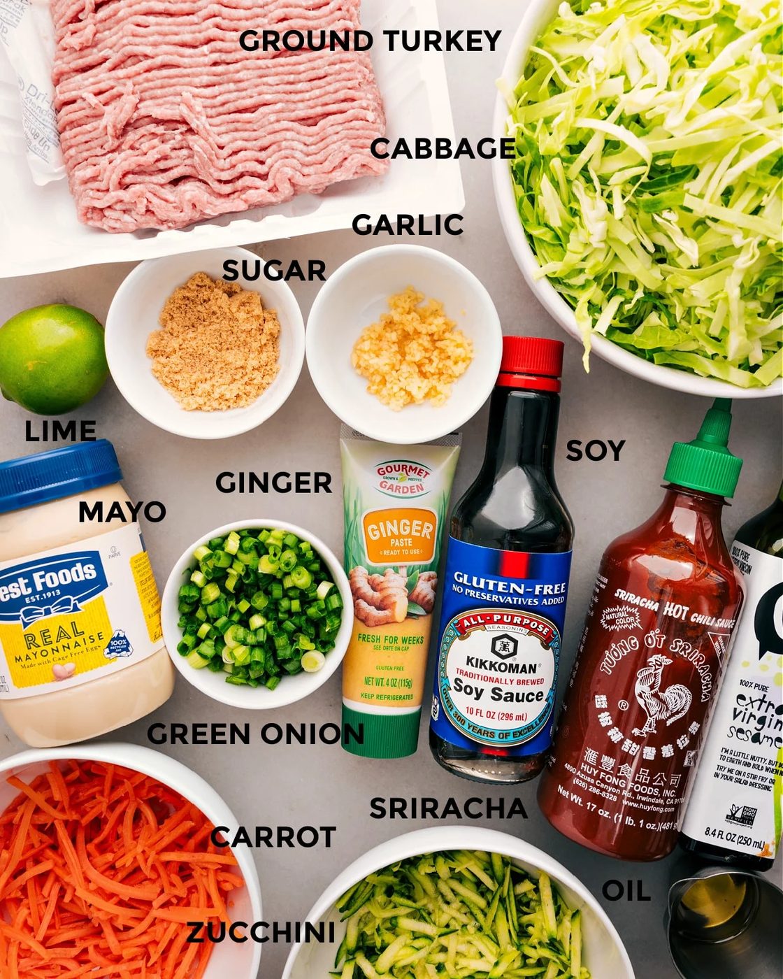 All the ingredients for this recipe are prepped and ready for straightforward assembly: meat, cabbage, garlic, sugar, mayo, ginger, soy sauce, sriracha, carrots, zucchini, and oil.