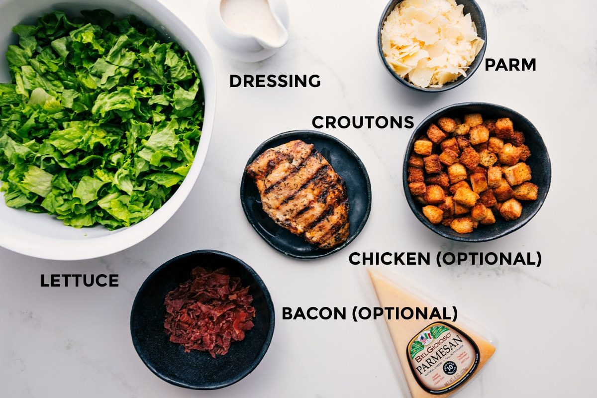 All the ingredients prepped and ready for straightforward assembly: lettuce, dressing, Parmesan, croutons, bacon, and chicken.