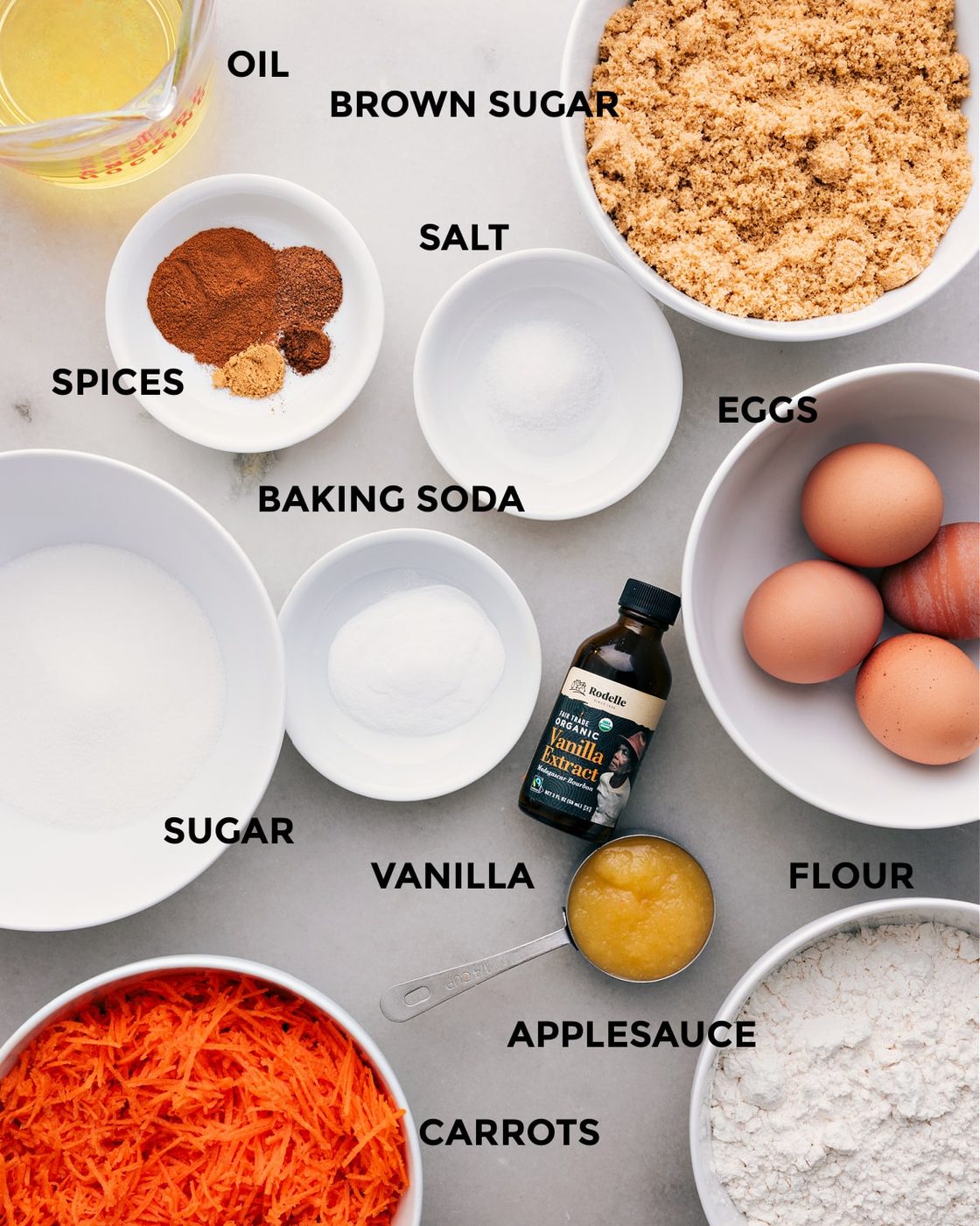 I’ve prepped all the ingredients for straightforward assembly—oil, brown sugar, eggs, salt, spices, baking soda, vanilla, sugar, flour, applesauce, and carrots.