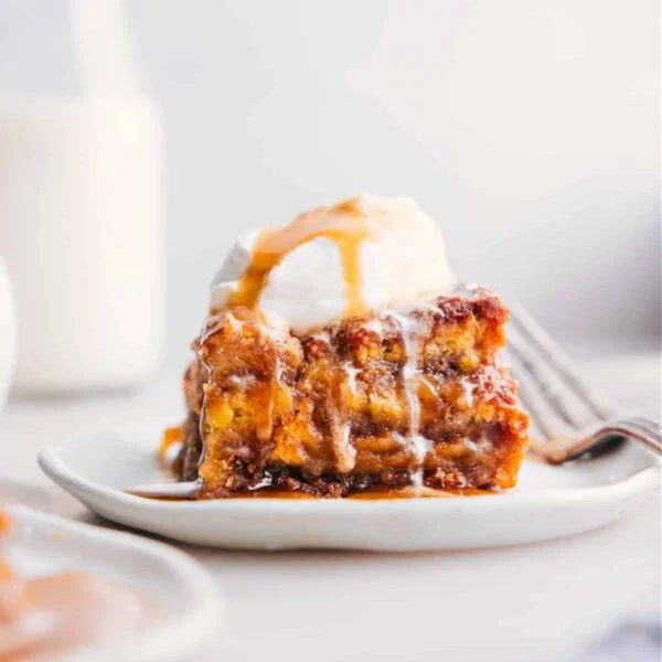 A slice of bread pudding topped with a scoop of ice cream, served warm as a satisfying dessert.