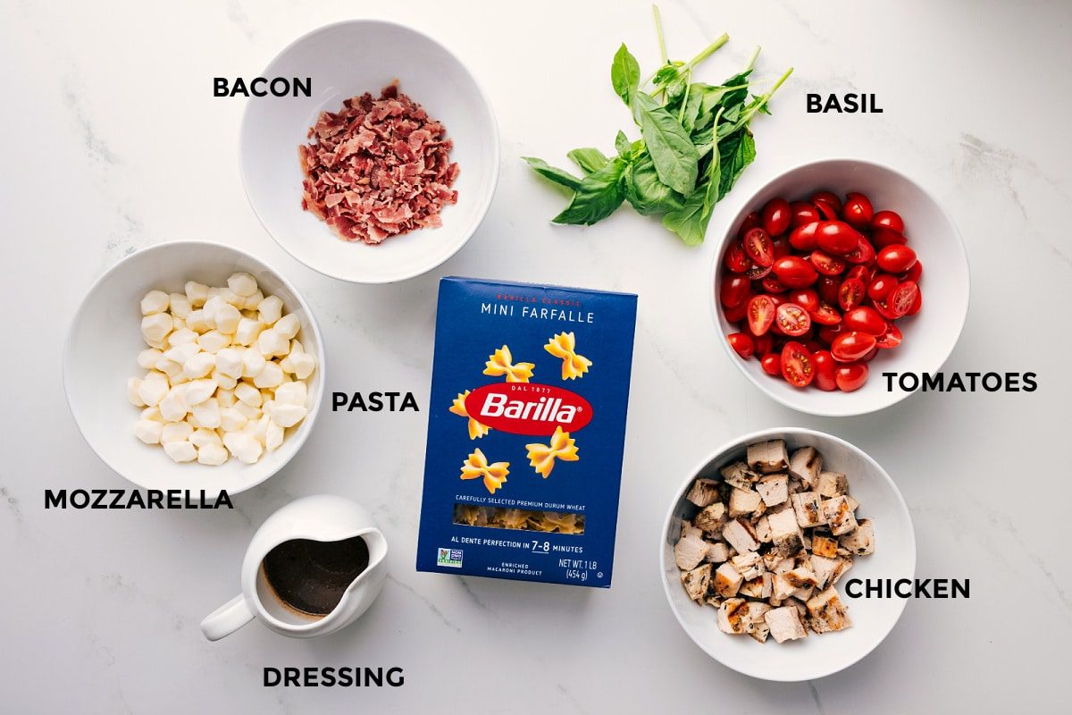 All the ingredients in this recipe prepped out for straightforward assembly including the bacon, mozzarella, dressing, pasta, chicken, tomatoes, and basil.