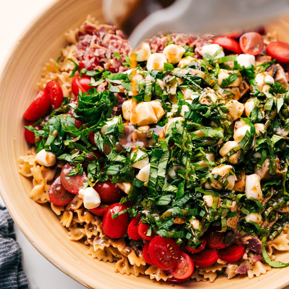 Dressing being poured over Caprese Pasta Salad in a large bowl before being tossed together.