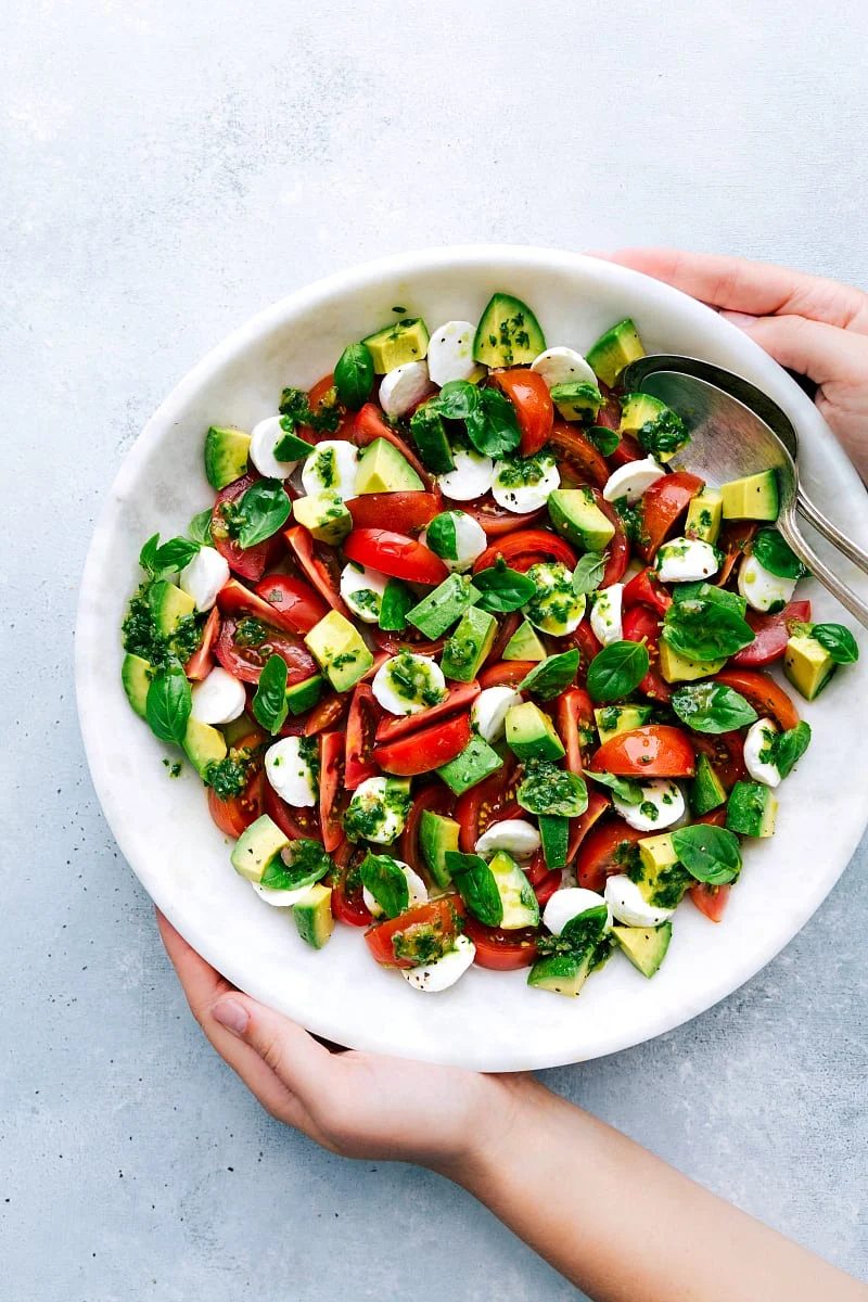 Caprese Salad in a bowl tossed with basil vinaigrette and topped with torn fresh basil leaves.