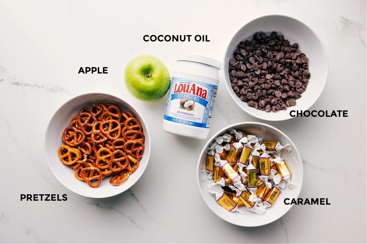 Ingredients in this recipe prepped out for straightforward assembly including the pretzels, apple, coconut oil, chocolate, and caramel.