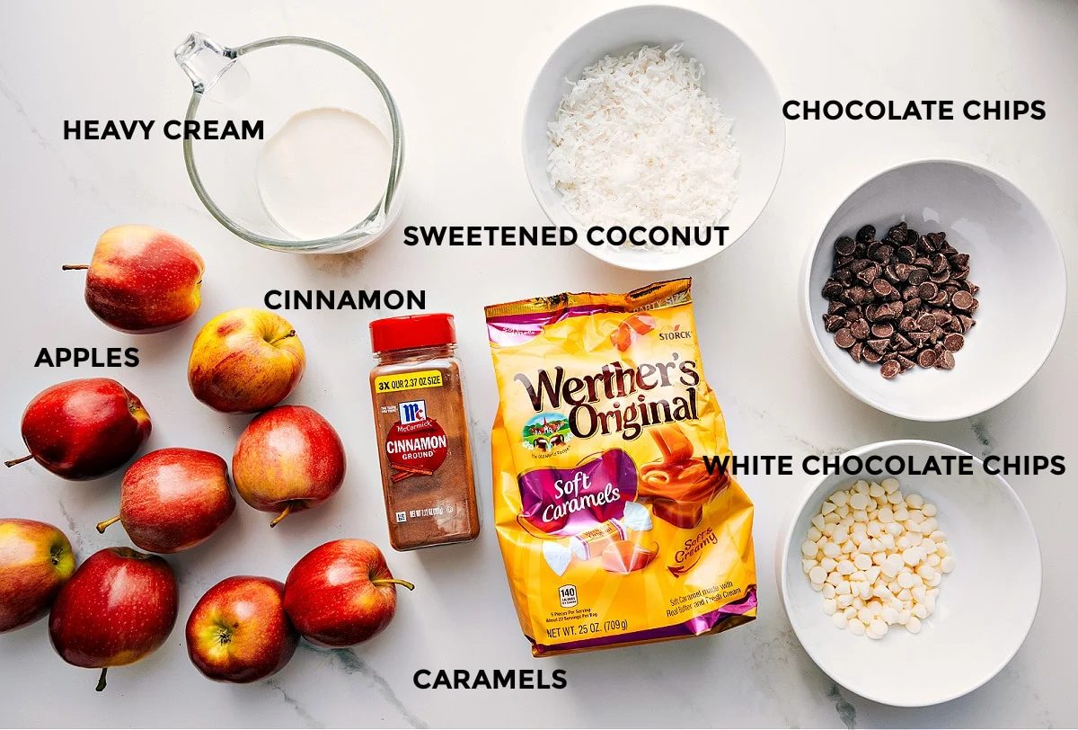 All the ingredients prepped and ready to assemble, including apples, heavy cream, cinnamon, sweetened coconut, caramels, chocolate chips, and white chocolate chips.