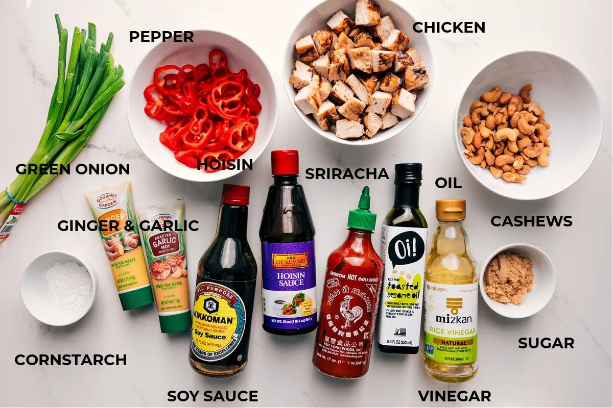 All the ingredients in this recipe prepped out for straightforward assembly including the green onion, cornstarch, ginger, garlic, soy sauce, sriracha, oil, vinegar, sugar, cashews, chicken, and peppers.