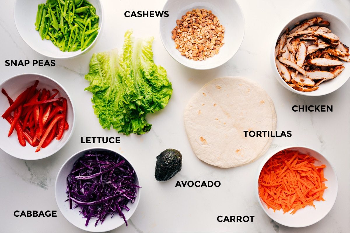 Ingredients in cashew chicken wraps prepped out for straightforward assembly including the snap peas, peppers, cashews, chicken, tortillas, carrot, avocado, lettuce, and cabbage.