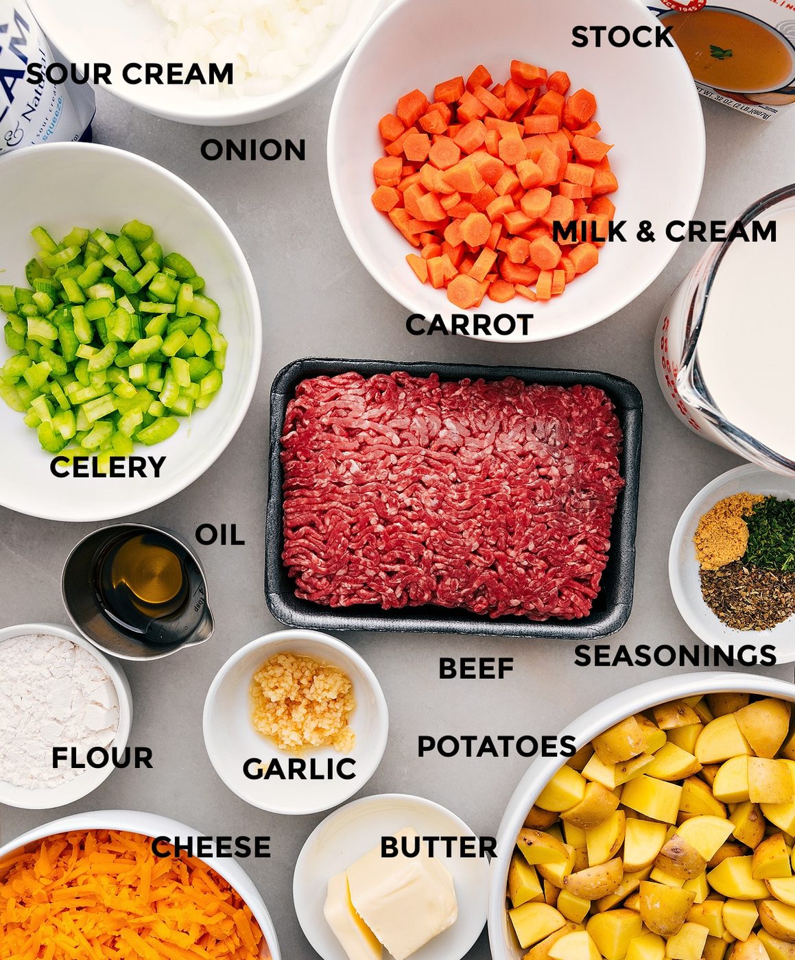 All the ingredients in this recipe including beef, seasonings, milk, cream, veggies, cheese, flour, and oil prepped out for straightforward assembly.