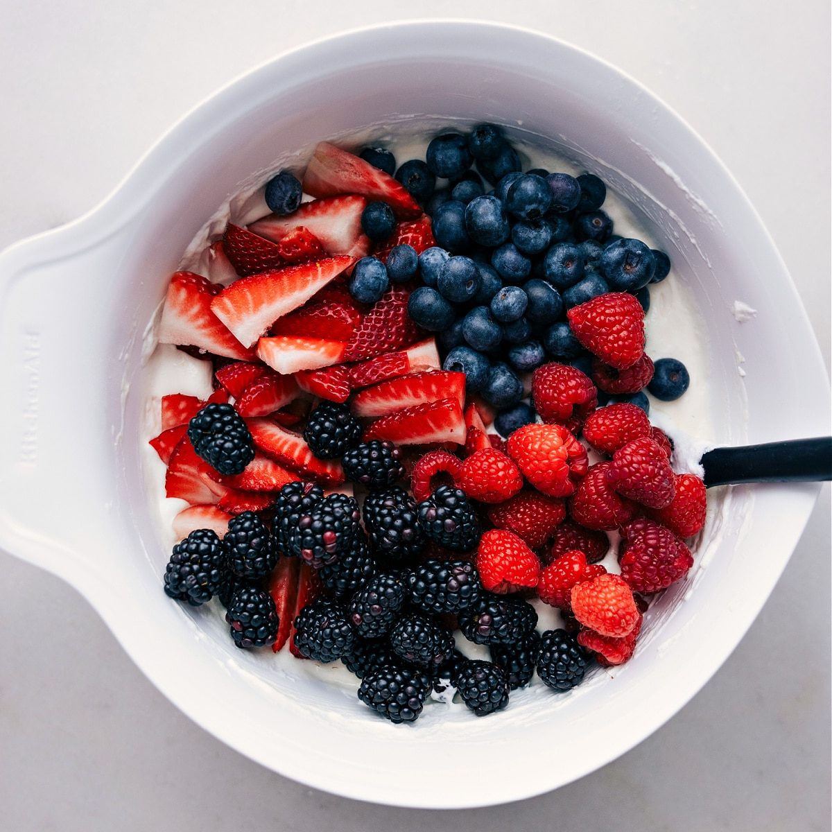 The berries being mixed into the creamy dressing layer.