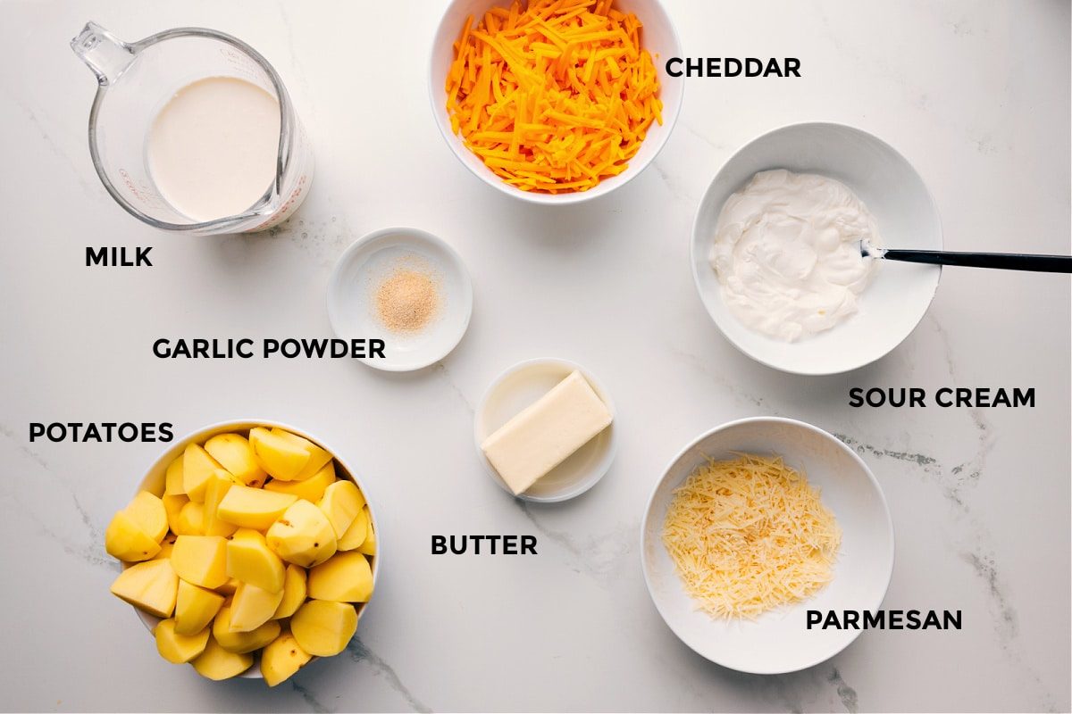 All the ingredients in this recipe prepped out for straightforward assembly including the milk, garlic powder, potatoes, butter, parmesan, sour cream, and cheddar.